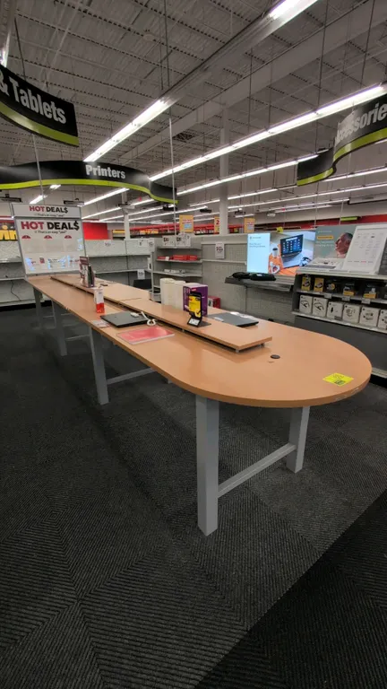 3-section laminate table. Features light woodgrain laminate top with rounded ends, center raised display riser, and integrated electrical outlets. Mou