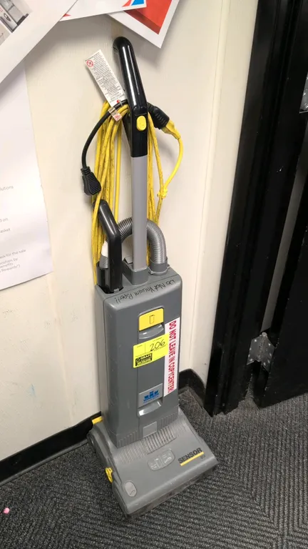 Windsor Sensor S12 commercial upright vacuum. Features 12" cleaning path, onboard flexible hose and wand attachment, and high-visibility yellow power