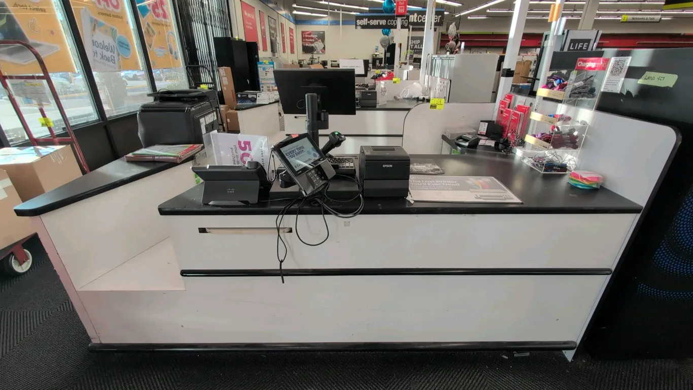Laminate checkout lane. Features black laminate countertop, white base with bumper trim, undercounter shelving, bag holder, and an overhead illuminate