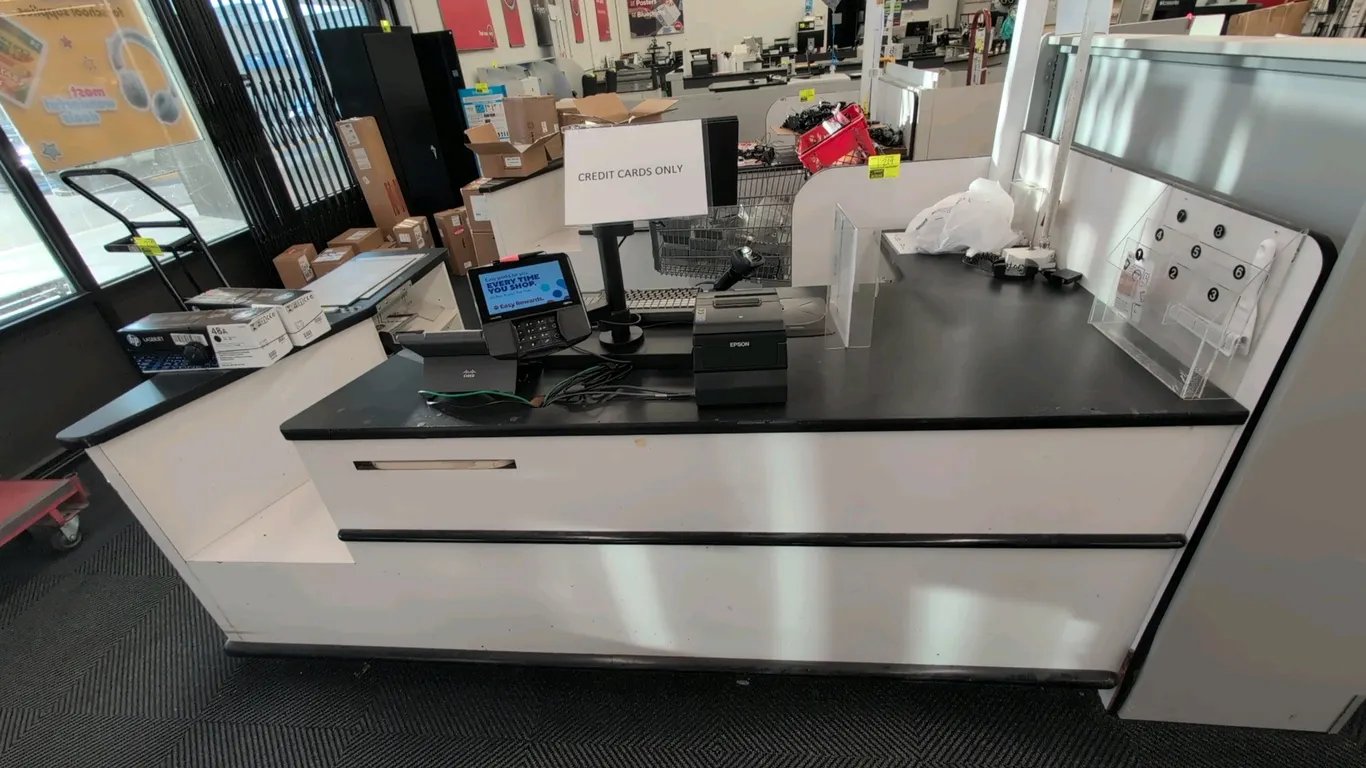 Laminate checkout counter lane. Features black laminate countertop, white base with protective bumper trim, under-counter storage shelving, bag holder