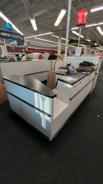 Laminate retail checkout counter lane with overhead lighted "Check Out" sign pole. Features black laminate countertops, white paneling, integrated sto