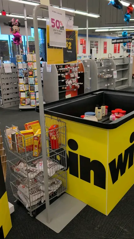 Metal adjustable floor sign stand. Features telescoping height adjustment, top sign hanging ring, and a flat rectangular metal base. Signage and surro