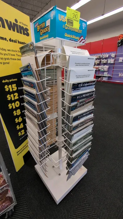 Metal portable merchandise rack. Features 4-sided multi-tier wire pockets, rotating carousel design, and top signage header. Mounted on a square base.