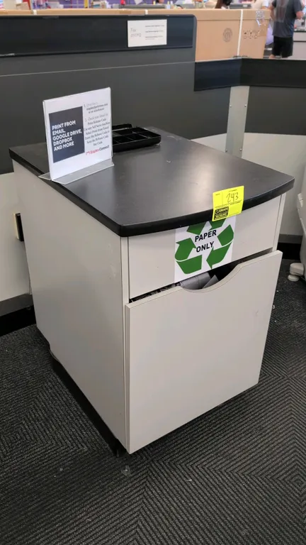 Laminate countertop waste and recycling cabinet. Features a black laminate top with drop-in cut-out access and a lower cabinet door housing an interna