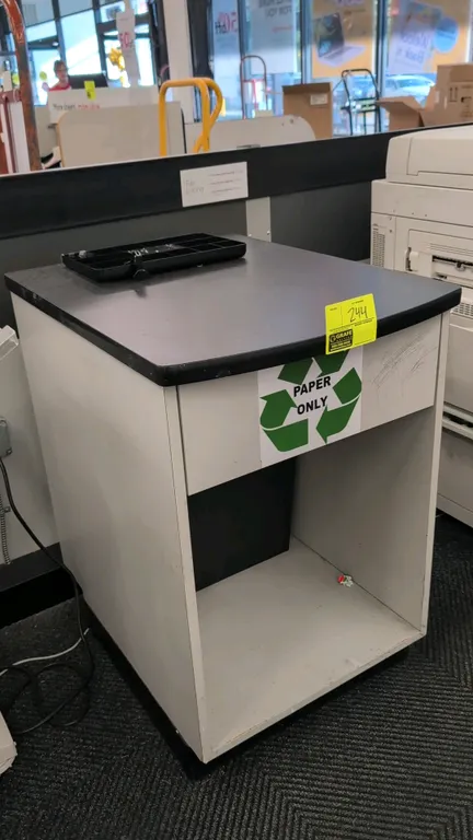 Laminate countertop cabinet with lower waste receptacle. Features a black laminate top, open lower storage compartment, and included black interior wa