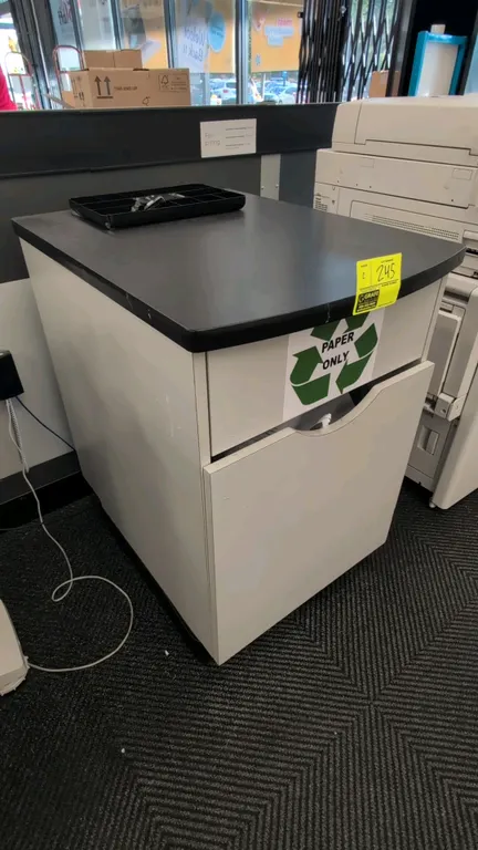 Laminate countertop waste bin cabinet. Features black laminate top, white cabinet base with drop opening, and interior waste receptacle. 2'x2'x3'. Con