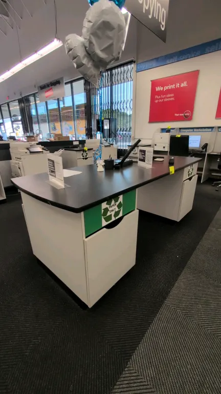 Laminate countertop workstation table. Features a black laminate work surface supported by two white pedestal bases with integrated pull-out recycling