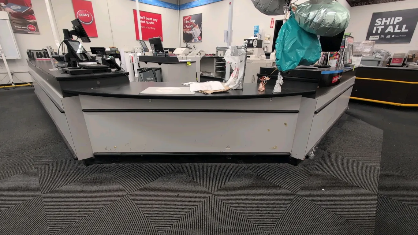 Laminate L-shaped service countertop with undercounter storage. Features black laminate countertop surface, multi-compartment lower open shelving, and