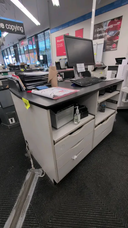 Laminate service counter with under-counter storage. Features a black laminate top with raised front ledge, white cabinet base, pull-out storage shelv