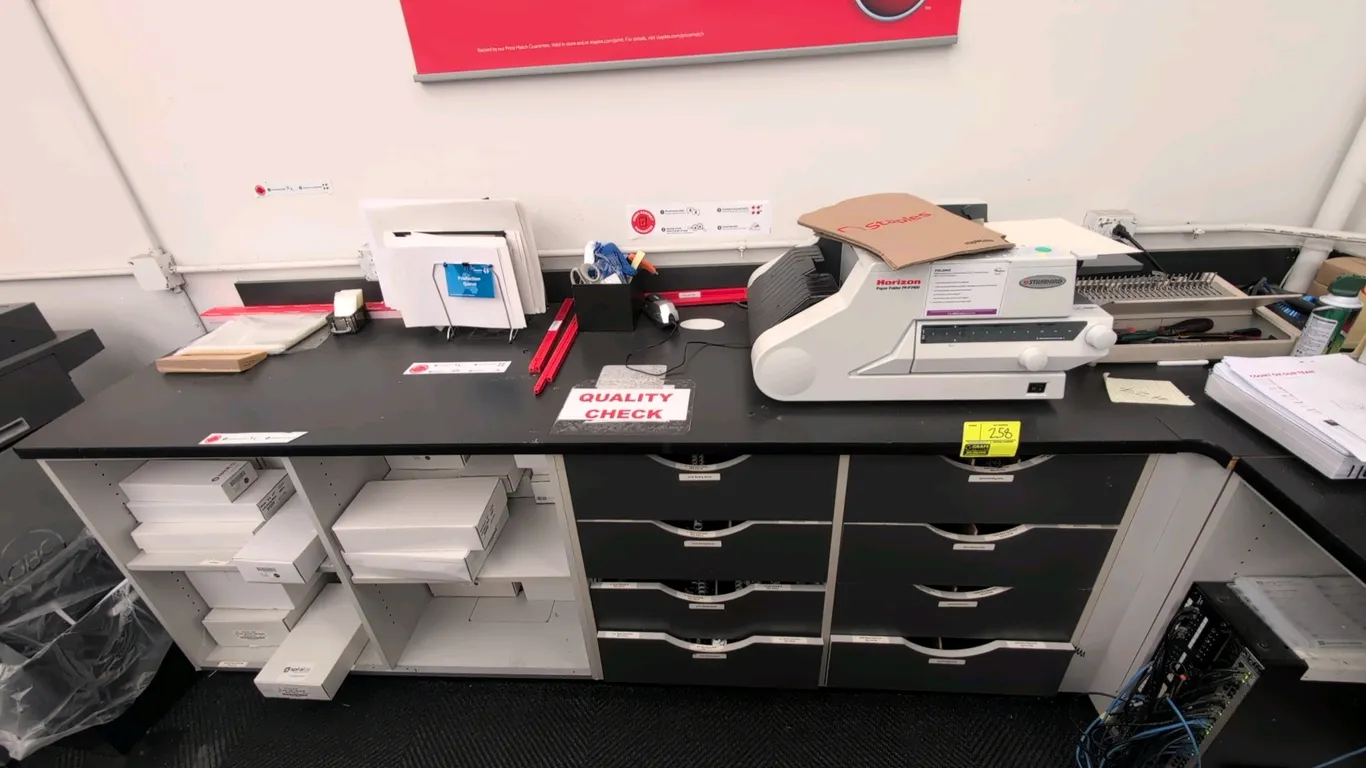 L-shaped laminate countertop workbench with under-storage cabinets. Features black laminate work surface, multiple lower storage compartments, adjusta