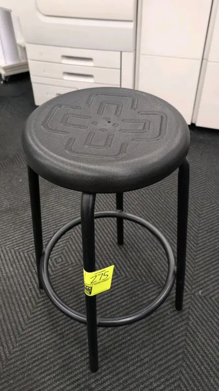 Foam cushioned stool. Features a molded black foam round seat with embossed geometric design and an integrated circular footrest ring. 27"H. Mounted o