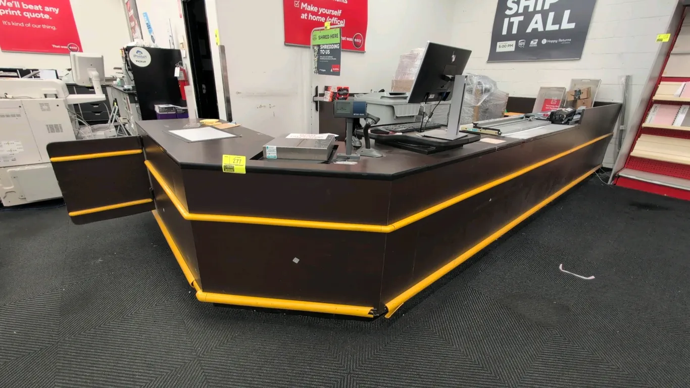 Laminate U-shaped service counter. Features dark brown laminate finish, yellow bumper trim, integrated swing access gate, and lower under-counter stor
