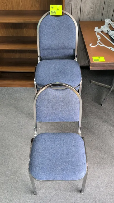 Cloth cushioned stacking chairs. Features blue fabric upholstered padded seat and backrest. Chrome-finish metal frame with protective floor glides.