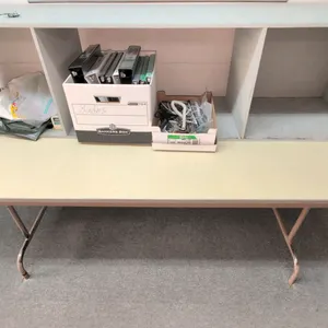 Laminate folding table. Features a neutral laminate top with protective edge trim. Mounted on a folding tubular metal base. Dimensions: 6' x 2.5'. Con