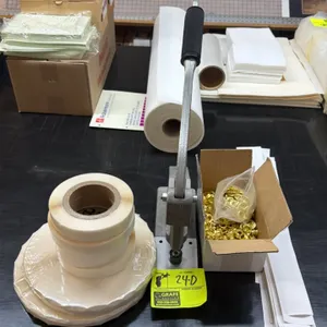 Manual grommet press and banner finishing supplies. Includes hand-lever brass ring press, box of brass grommets, rolls of double-sided tape, and paper