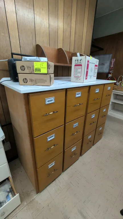 Laminate storage cabinet with wood upper shelf. Cabinet features a white laminate top with backsplash, 12 pull drawers with brass-tone hardware, and m