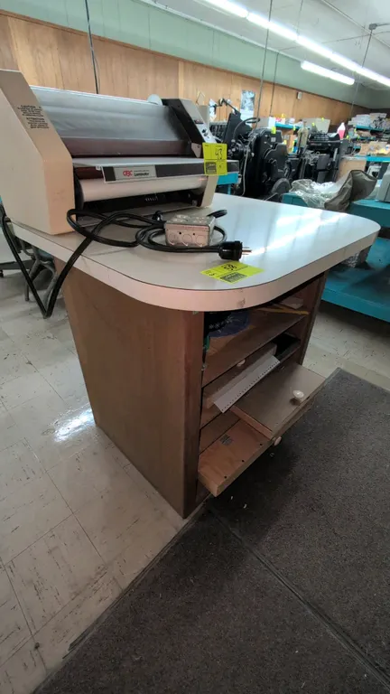 Laminate countertop storage cabinet. Features a white laminate top with rounded corners, wood-finish base, under-counter storage with pull-out shelves