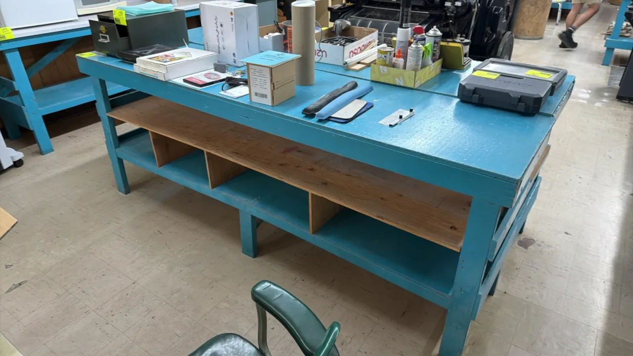 Wooden work table. Features a blue painted finish and integrated lower shelving with divided compartments. 8'L x 2'W x 3'H. Contents not included.