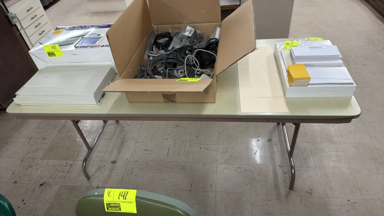 Laminate folding table. Features a laminate top with metal edge trim. 6'L. Mounted on folding tubular metal legs. Contents not included.