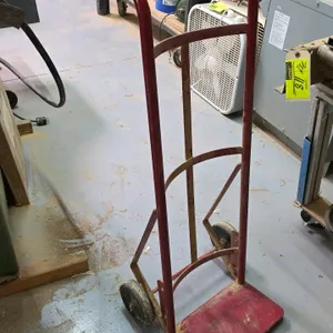 Hand truck. Features red tubular steel frame, continuous loop handle, curved cross braces, fixed nose plate, and (2) solid wheels.