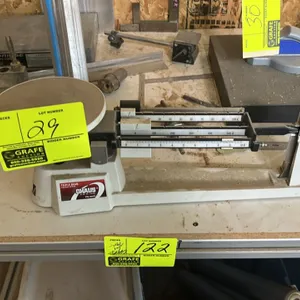 Ohaus 700/800 Series mechanical triple beam balance scale. Features a round metal weighing platform, notched tiered beams with sliding poise weights, 