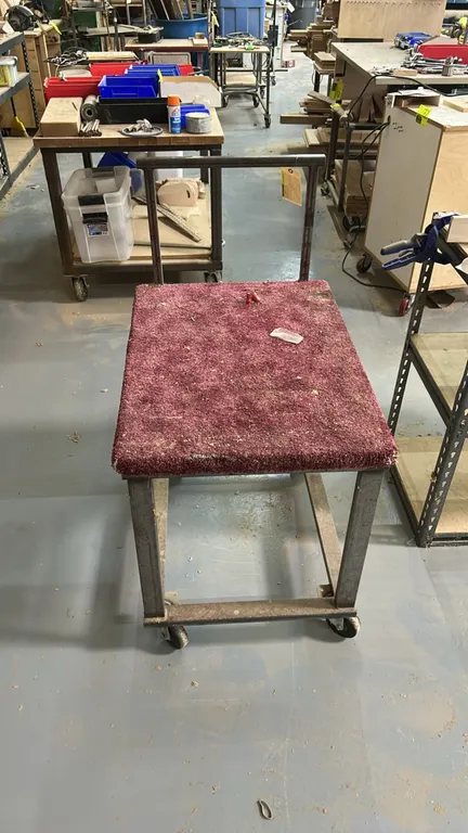 Metal shop cart. Features a carpet-padded top platform and integrated push handle. 32"H. Mounted on swivel casters.