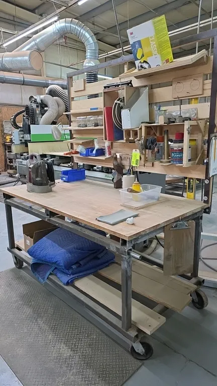 Mobile wood top workbench with overhead organizer rack. Features upper wooden shelving system and lower storage shelf. Includes visible tabletop and s