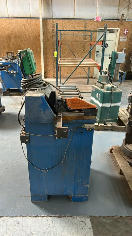 Mechanical cut-off saw. Features an integrated infeed roller conveyor, top blade guard clamp assembly, rear-mounted electric motor, and top push-butto