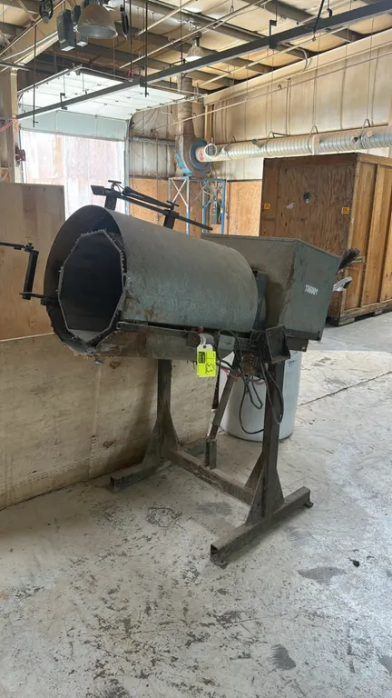 Industrial rotary barrel tumbler polisher. Features an octagonal interior tumbling chamber with media, enclosed drive housing, and manual tilt adjustm