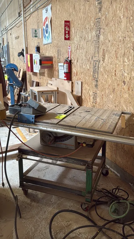 RIDGID TS2412 D table saw. Features front safety power switch, blade height and bevel adjustment handwheels, and front guide rail. Mounted on a mobile
