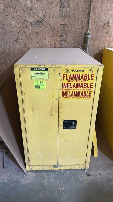 Justrite Sure-Grip flammable liquid storage cabinet. Features dual-door construction, flush paddle latch handle, and safety warning labels. Yellow fin