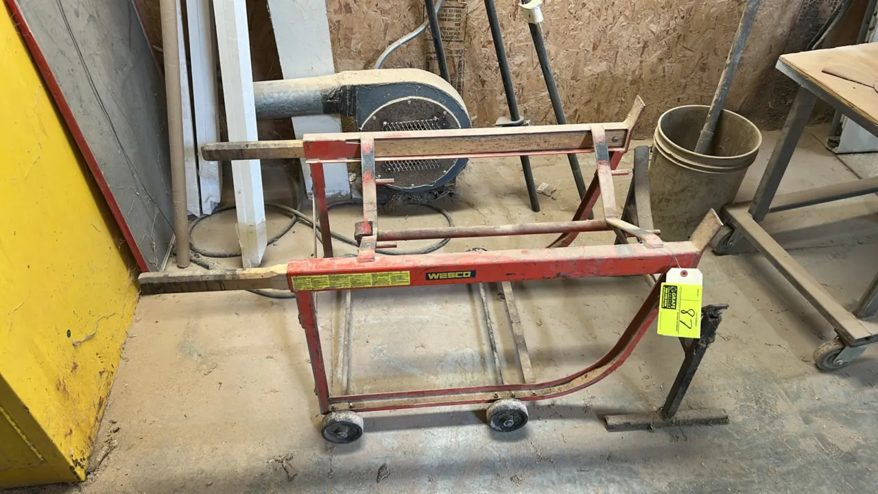 Wesco 55-gallon drum cradle. Features steel construction, handles, and rocker frame for drum loading and dispensing. Mounted on 4 wheels.