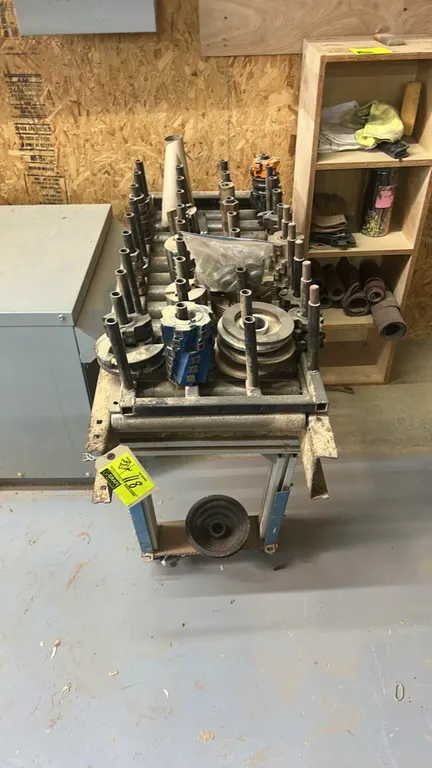 Mobile tooling rack with assorted woodworking shaper cutters, moulder heads, interchangeable tooling arbors, and 4-tier wood storage shelf. Features v