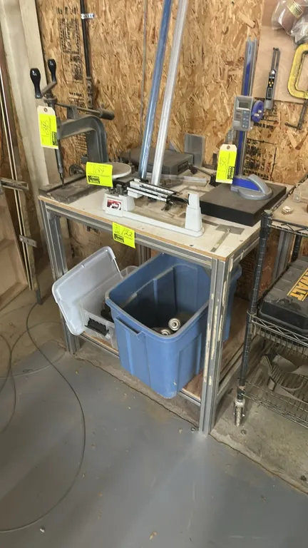 Extruded aluminum 2-tier work table. Includes metal gravity conveyor rollers, machinist combination square, ruler, and assorted bin contents on lower