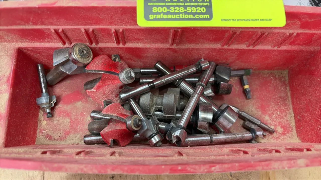 Assorted router bits and woodworking supplies. Includes various profile router bits in a red plastic storage bin, a roll of sandpaper, Titebond II woo
