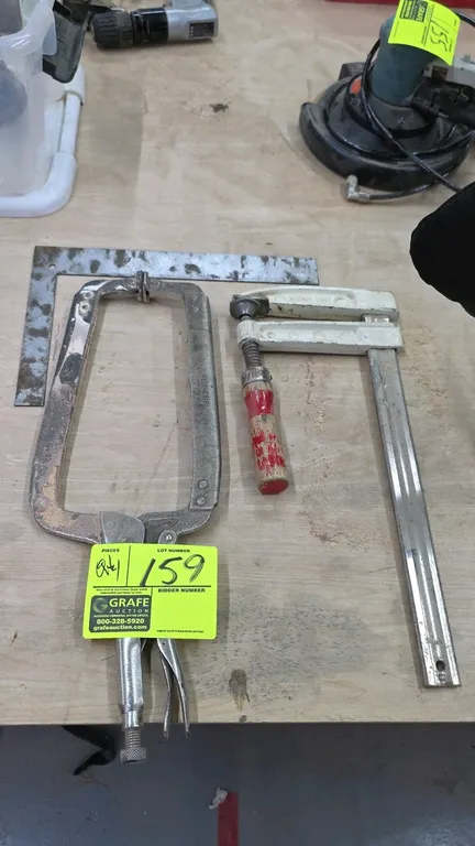 Assorted hand tools. Includes Vise-Grip locking C-clamp, F-style bar clamp with wooden handle, and metal framing square.