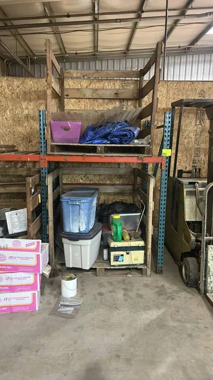 Metal teardrop pallet racking. Features blue upright frames and orange cross beams. Dimensions: 58" x 48". Contents, crates, pallets, and surrounding