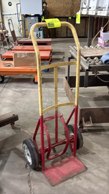 Metal 2-wheel hand truck dolly. Features tubular steel frame, loop handle, curved crossbars, rigid toe plate, and two solid rubber tires.