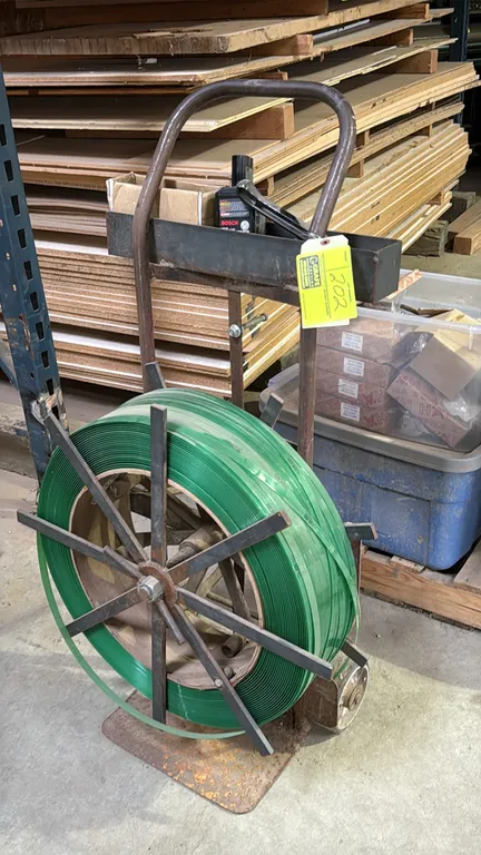 Strapping dispenser cart. Features tubular steel frame, upper tool storage tray with manual tensioner tool, and a roll of green poly strapping. Mounte