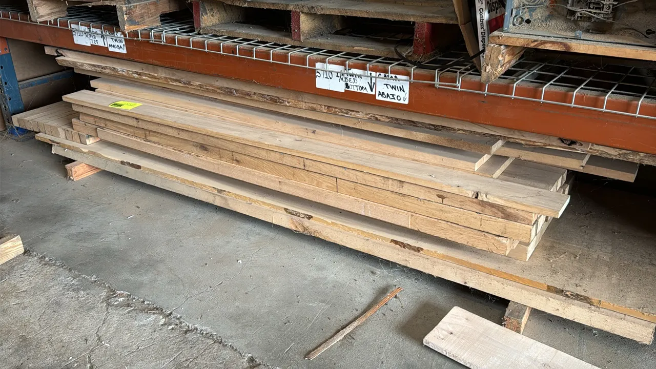 Assorted wood boards and lumber. Features various lengths, widths, and thicknesses stacked on wooden skid base. Pallet racking and overhead items not