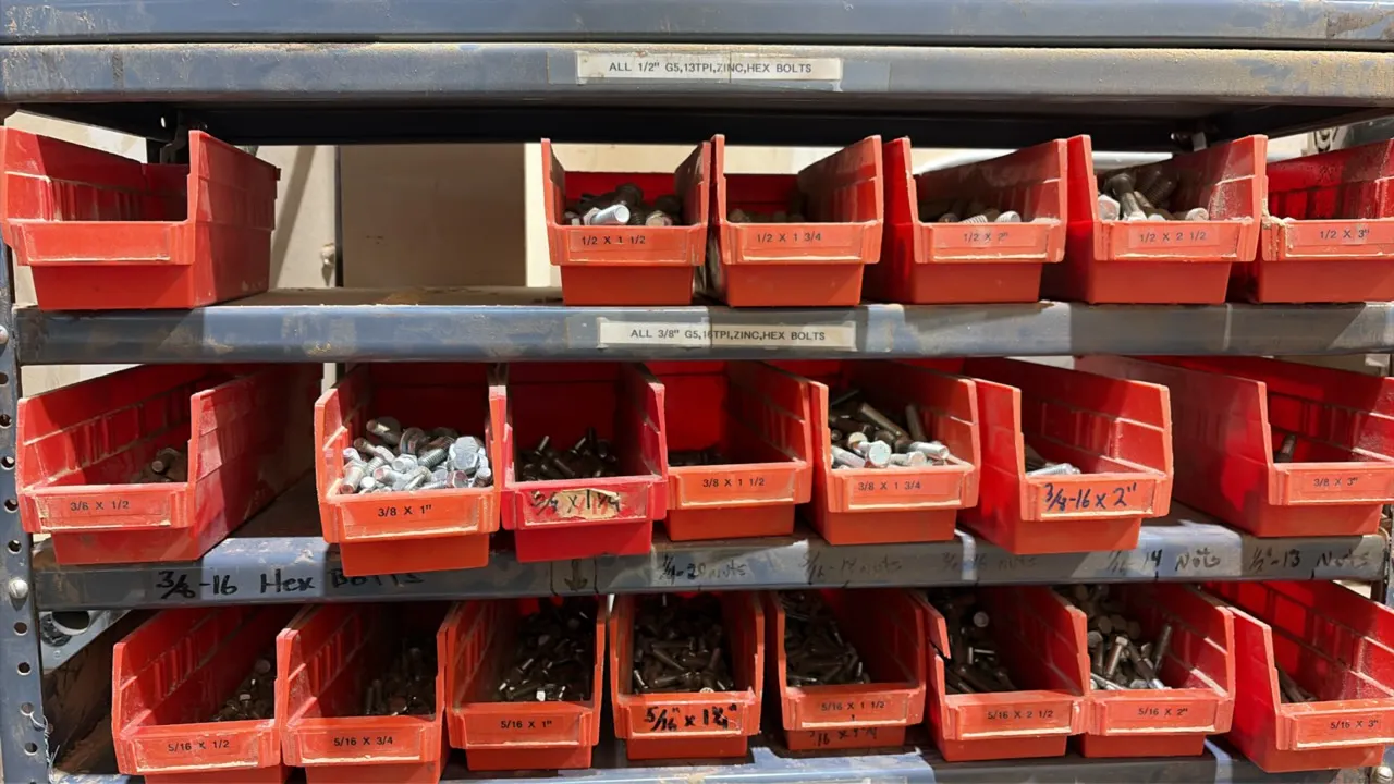 Metal 12-tier parts rack. Includes assorted plastic and cardboard storage bins containing hardware, bolts, sockets, and hand tools. 3' x 12" x 75".