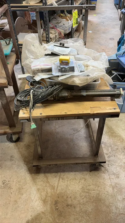 Metal utility cart with assorted parts. Features welded tubular steel frame, wood top surface, push handle, and 4-wheel caster base. Includes linear a