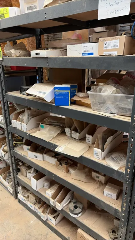 Assorted machine parts and electronic components. Includes boxed inventory, hardware, wiring, and various industrial replacement parts across 7 shelf