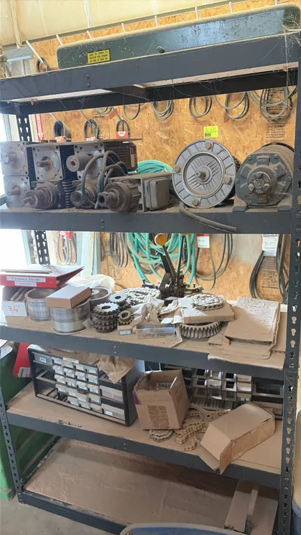 Metal storage rack with assorted motors and parts. Includes electric motors, gearboxes, sprockets, roller chains, hardware, and multi-drawer small par
