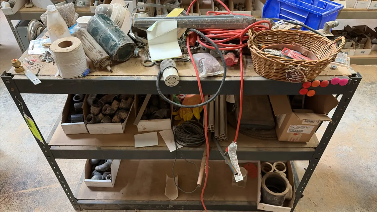 3-tier metal storage rack with assorted miscellaneous parts. Features steel frame construction with board decking. Includes assorted plumbing fittings