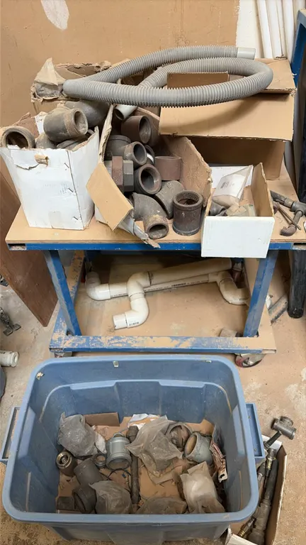 Metal four-wheel utility cart. Includes assorted pipe fittings, PVC connectors, flexible hose, plastic tote, and related parts. Blue metal frame const
