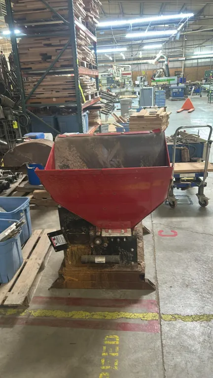 Stationary electric chipper and granulator. Features red top-loading feed hopper chute with rubber baffle guard, curved directional discharge chute, a