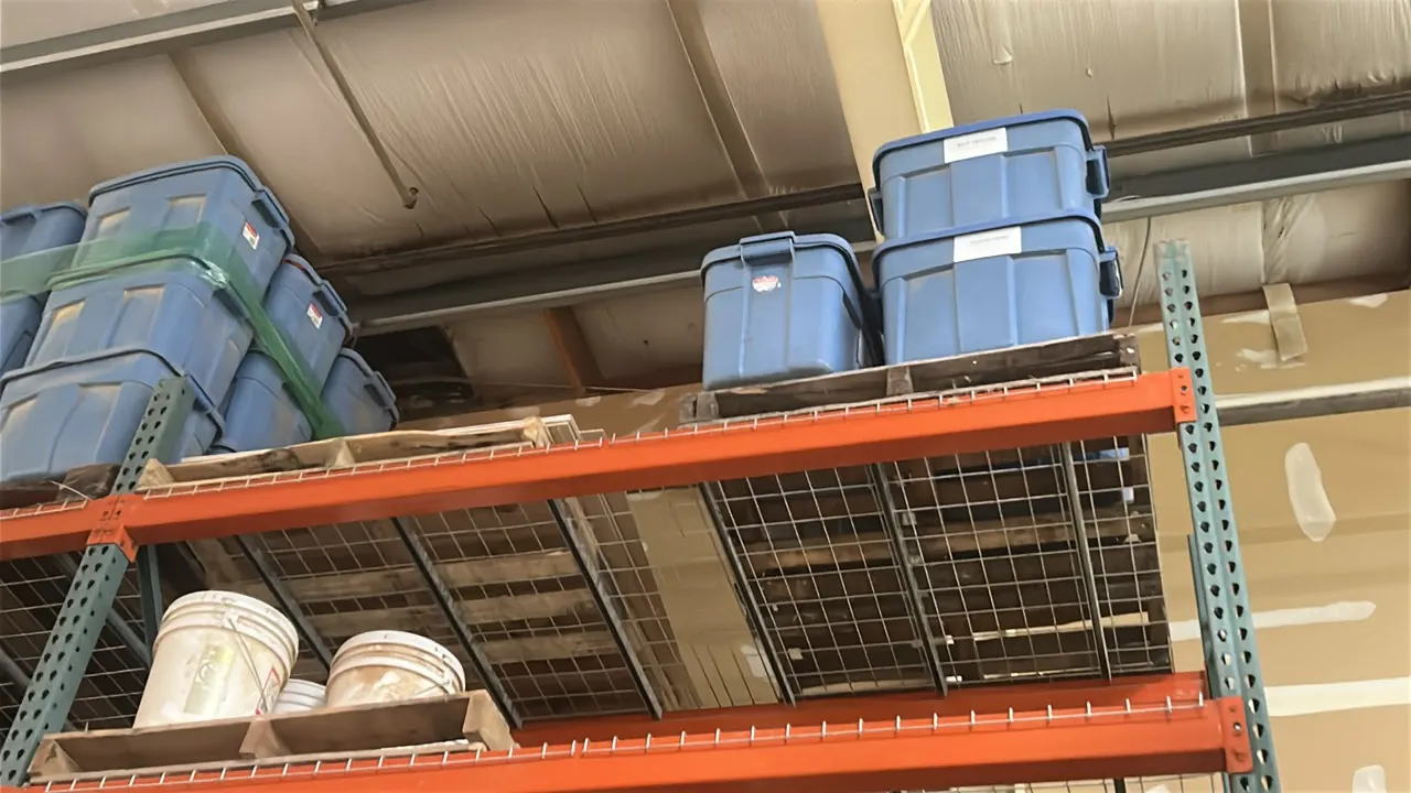 Assorted plastic storage totes and circular buckets. Includes blue rectangular storage totes with lids and white plastic round buckets located on uppe