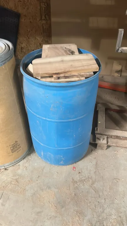 Industrial drums. Includes blue plastic open-top drum containing assorted wood cutoffs and fiber drum fitted with a yellow faucet.