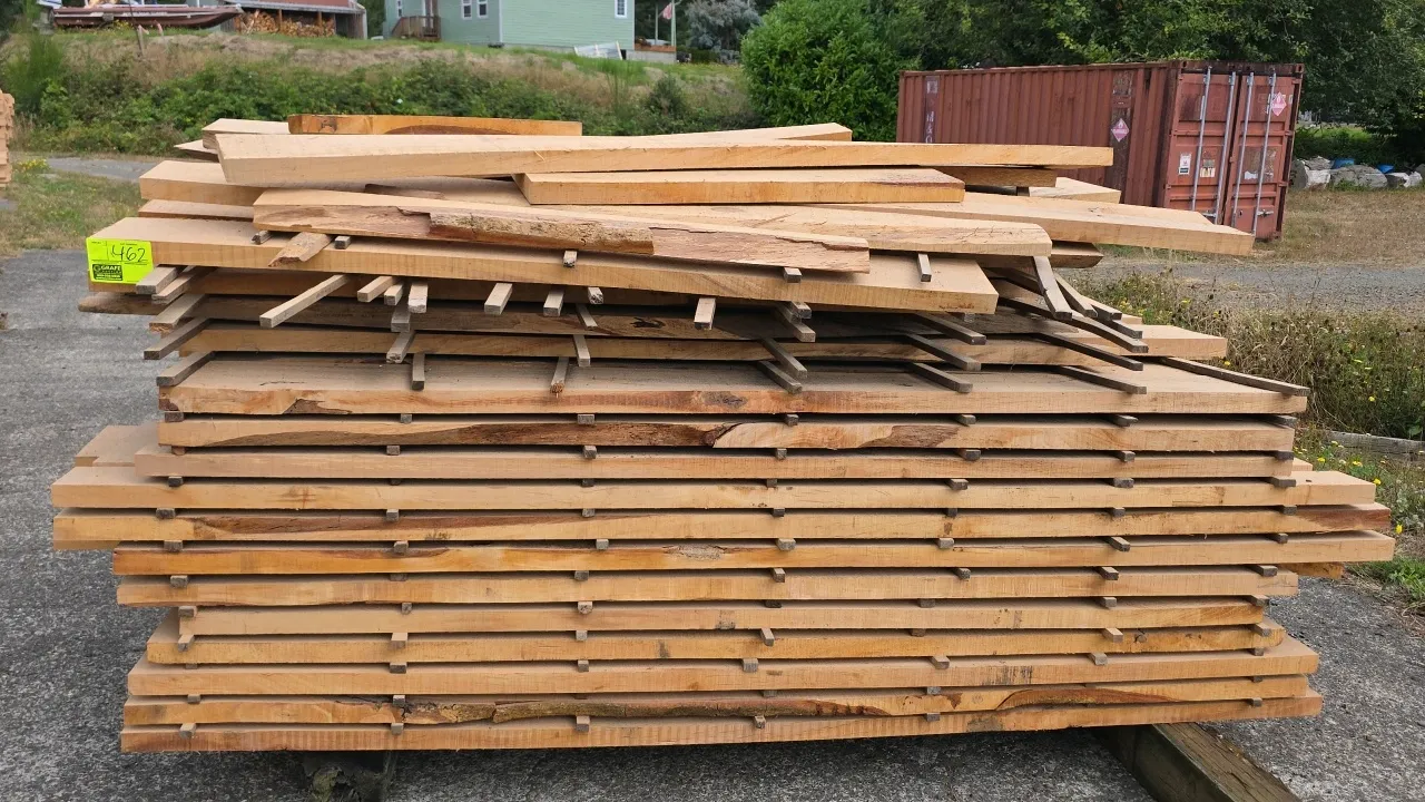 Stack of alder wood lumber. Features rough-sawn and live-edge boards stacked with stickers. Dimensions: Approx. 7' to 8'L x 1.5"T. Background items no